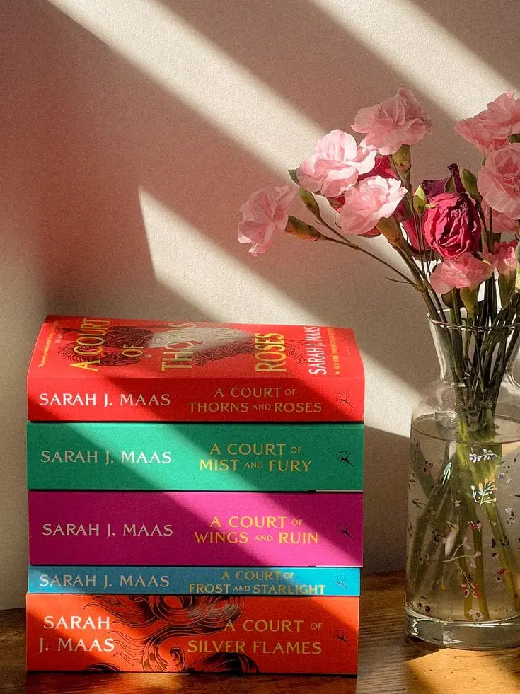 stacked ACOTAR books with flowers in window light