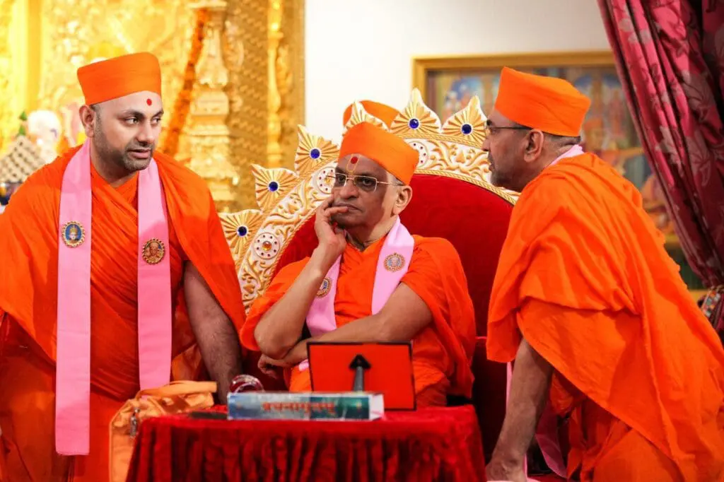 Hindu monks in orange robes speak during indoor ceremony