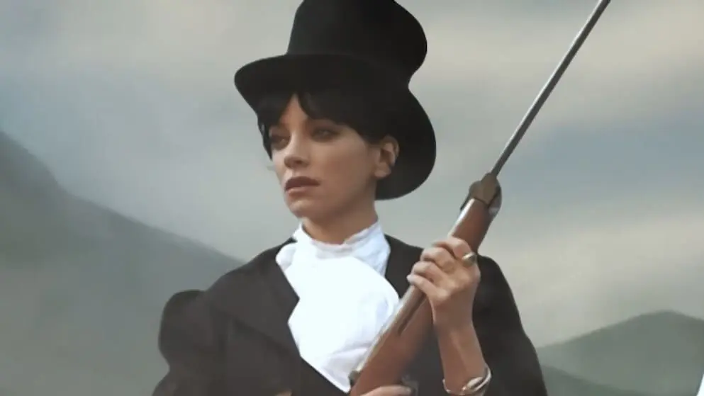 Lily Allen in a top hat holding a rifle in a staged scene