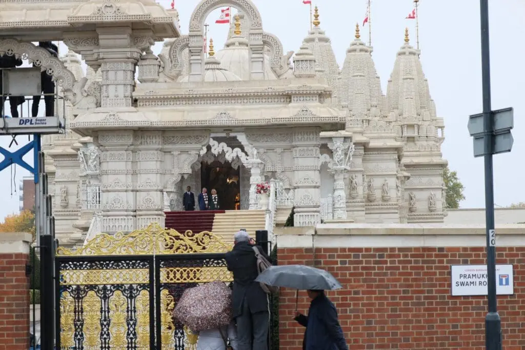 Neasden Temple entrance in rain with umbrellas at the gate
