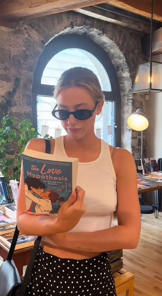 reader holds a book by a café window with sunglasses