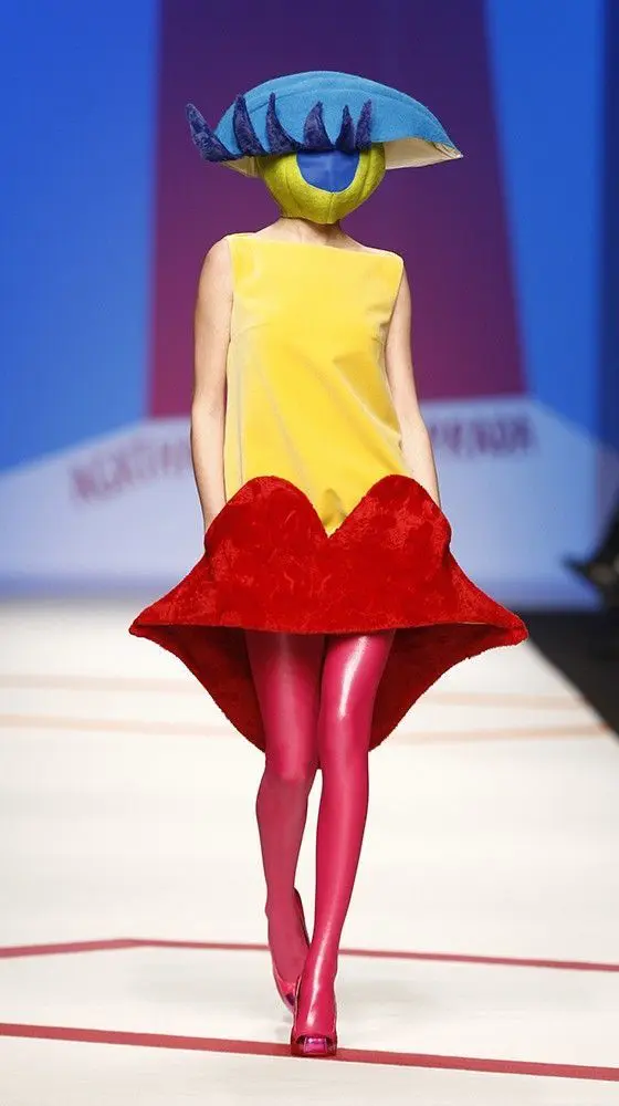 Surreal runway look with eye hat, yellow dress and red sculpted skirt