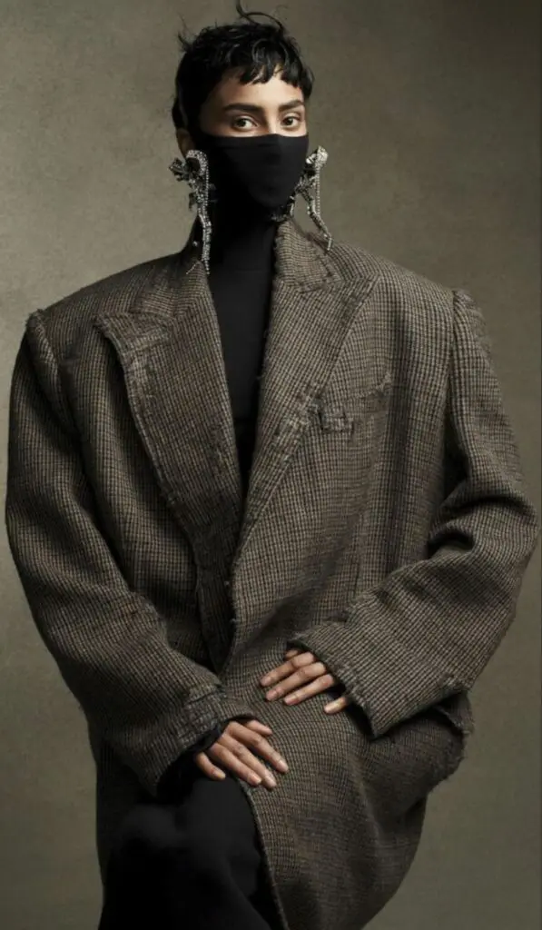 Oversized tweed coat with black face covering and statement earrings