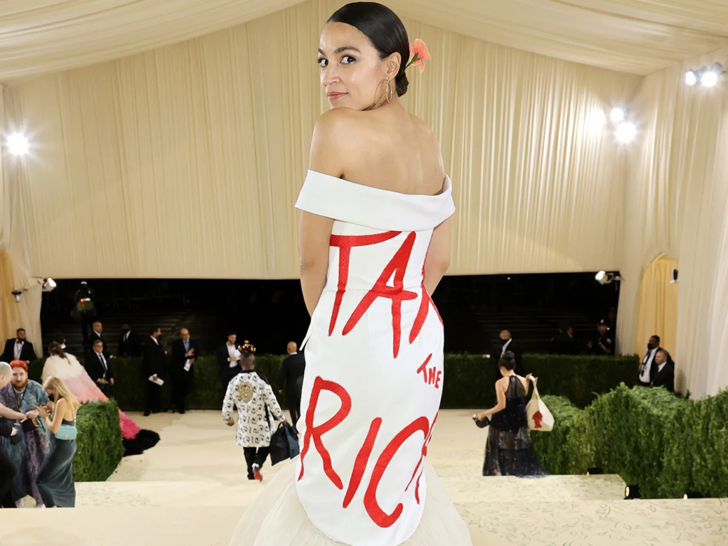 White off-shoulder gown with red “TAX THE RICH” text at gala