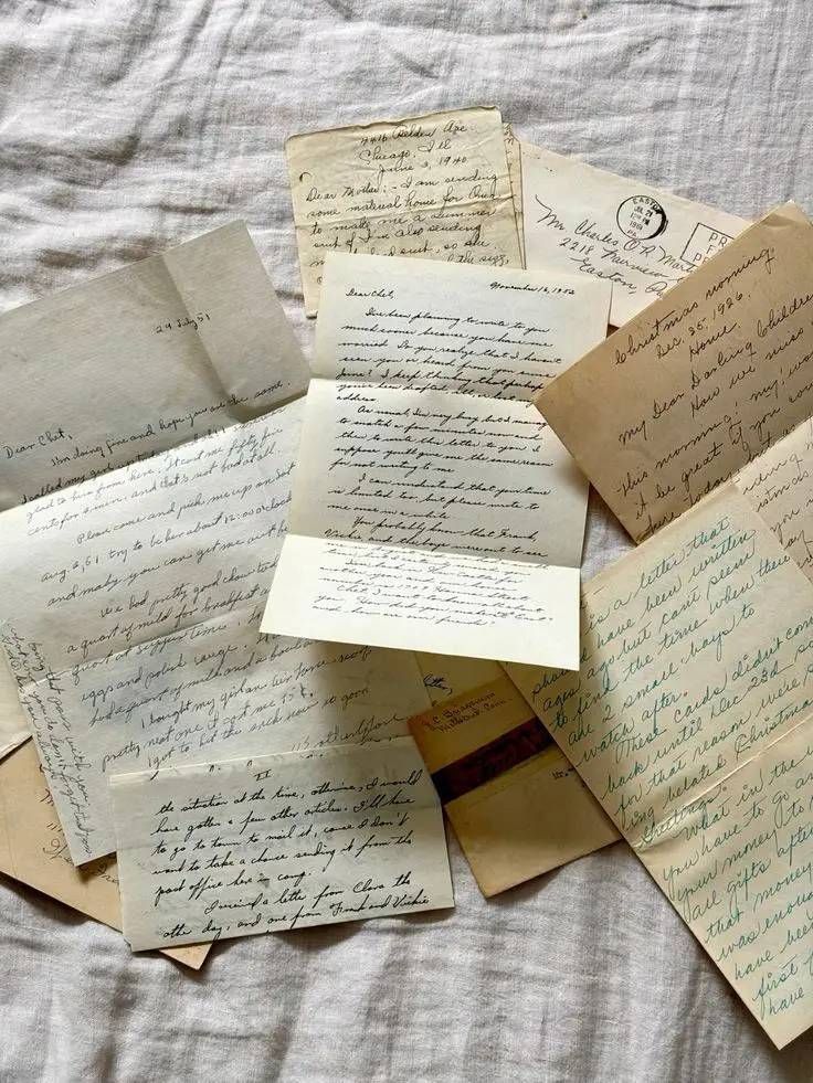 Handwritten letters and postcards scattered on linen bed