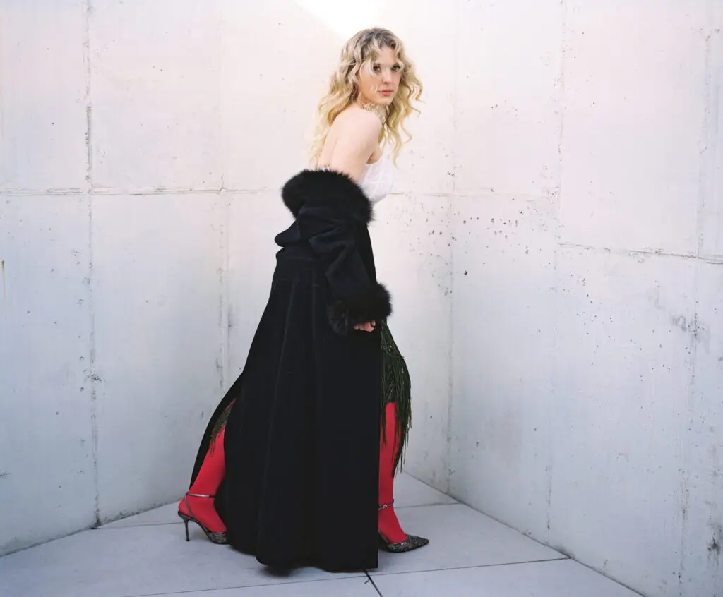 Relaxed yet commanding, Carson Allen reclines in a white dress on a leather sofa, embodying quiet confidence and modern editorial elegance.