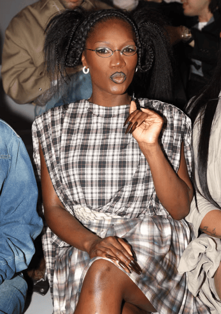 Doechii with bold pigtails, circular glasses, and defined lips at fashion show