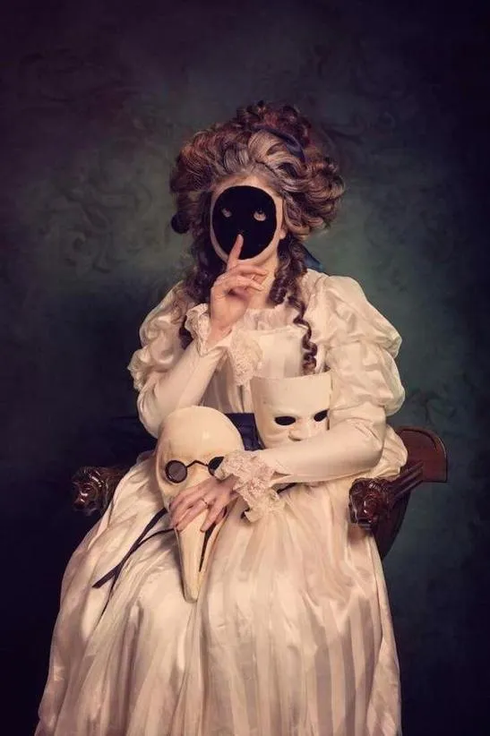 Close-up of a woman holding a black mask with two eye holes in front of one eye, highlighting performance of identity